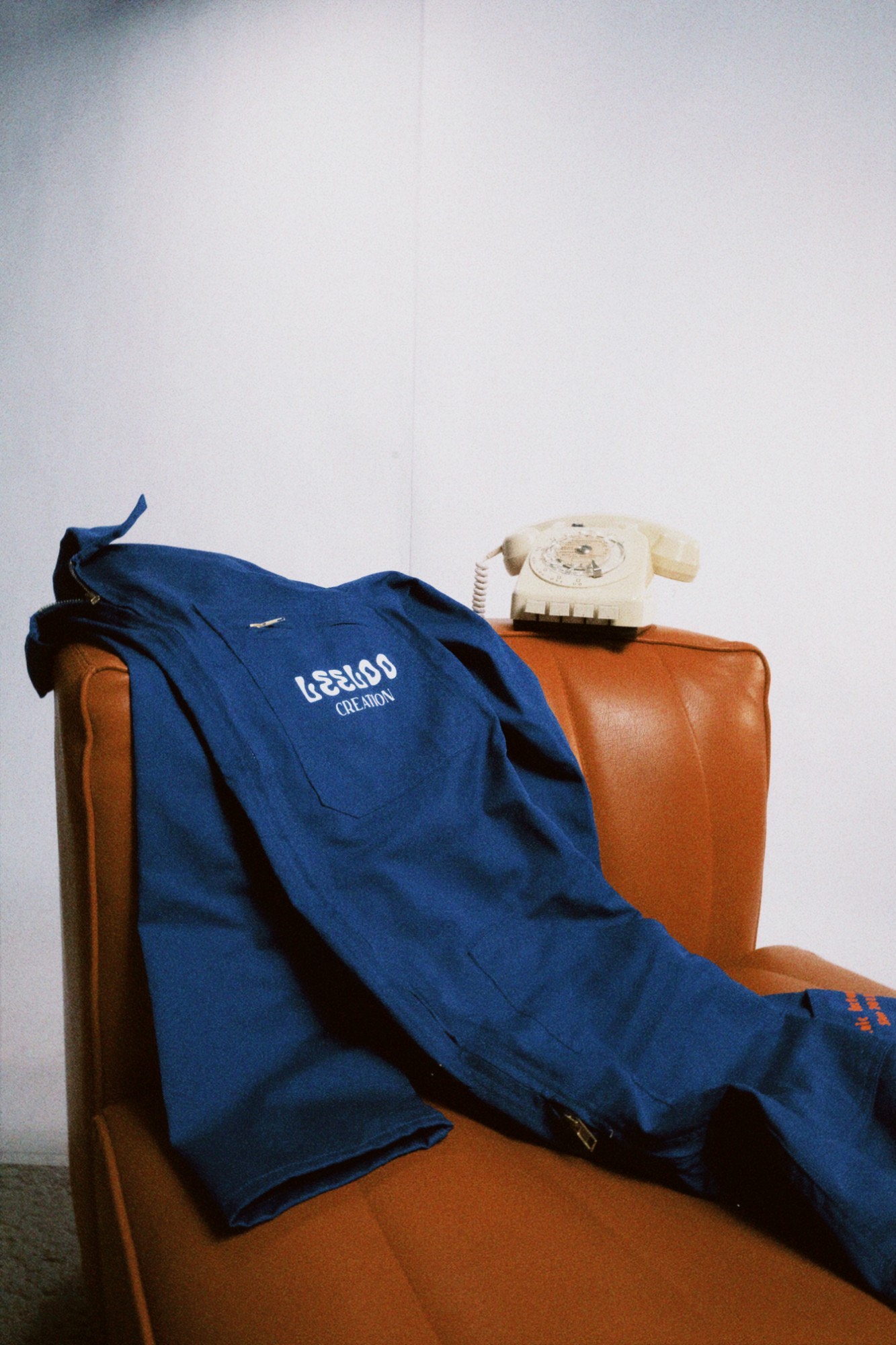 Leeloo Création workwear jacket resting on an orange leather armchair, next to a vintage telephone